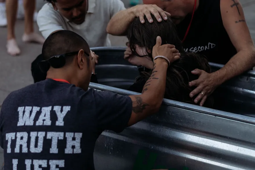 Men laying hands in prayer over someone in the baptism tank.