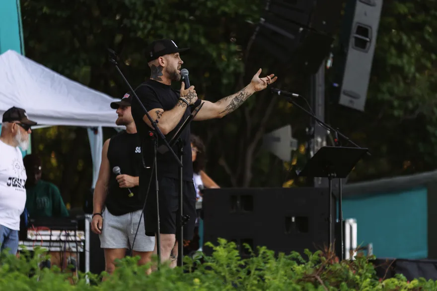 A speaker calling men forward with his arm outstretched toward the crowd.