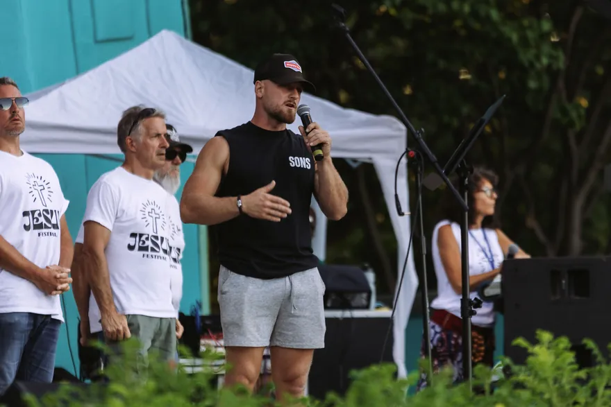 A man sharing his testimony into a microphone with other men standing behind him.